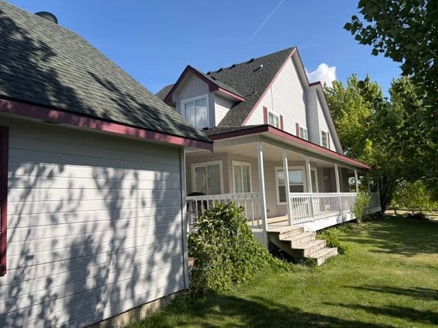 Charming two-story house with porch, surrounded by greenery under a clear blue sky.