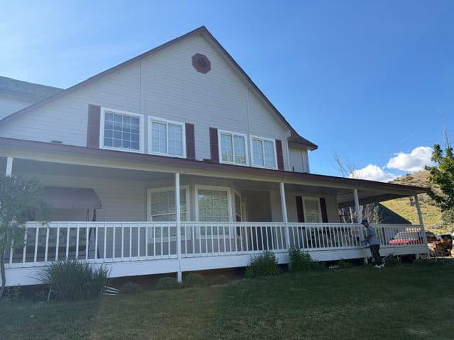 Large two-story house with porch, white siding, and red shutters under a blue sky.