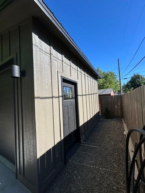Side view of a modern gray shed with a black door and clear blue sky background.