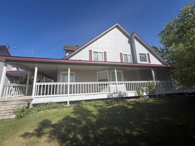 Two-story house with a covered porch and a green lawn under a clear blue sky.