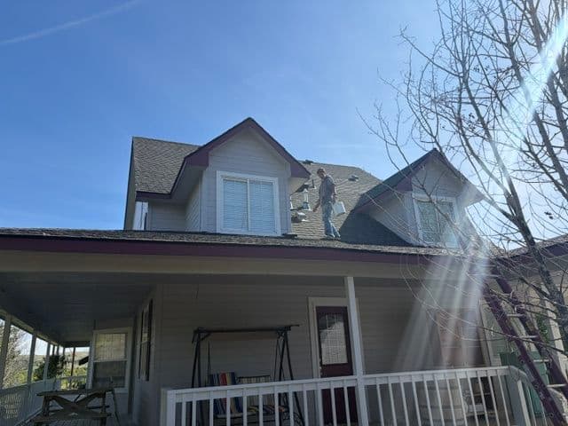 Man repairing roof on a house under clear blue sky, showcasing home maintenance.