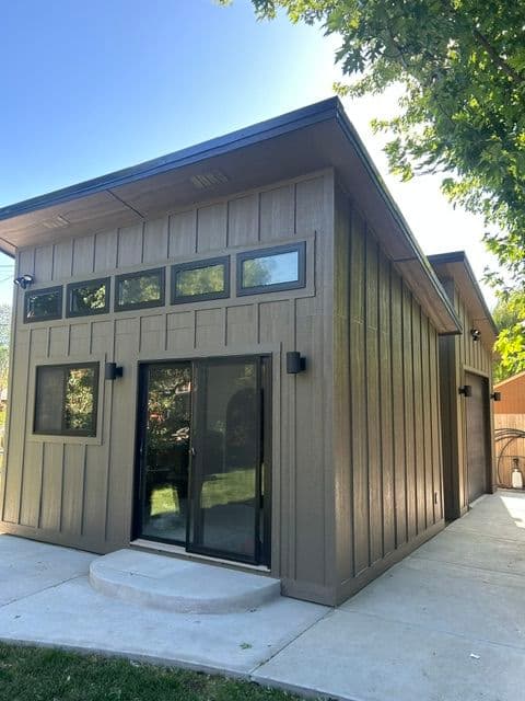 Modern outdoor shed with large windows and sliding door, surrounded by greenery.