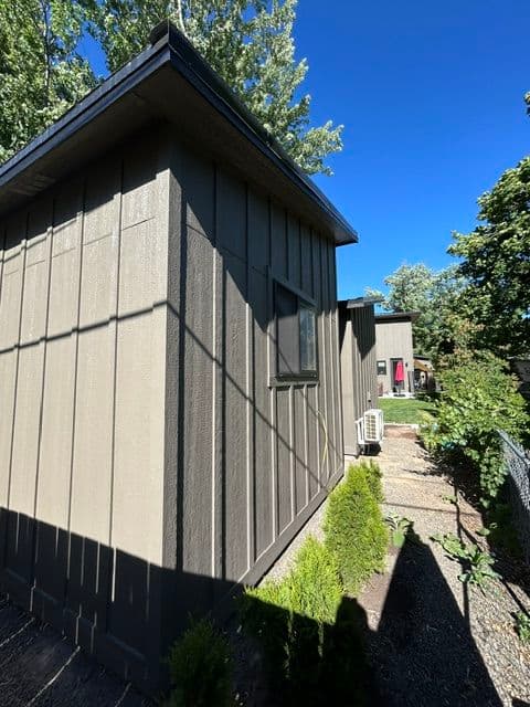 Modern detached shed with greenery and clear blue sky in background. Ideal for outdoor storage.