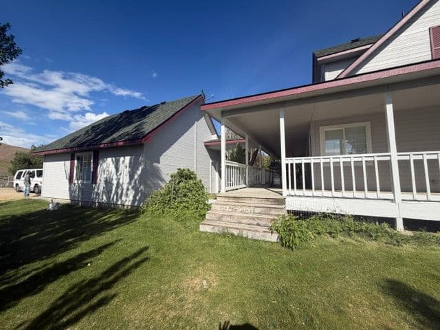 House exterior with solar panels, green grass, and a porch under a blue sky.