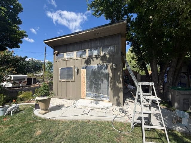 House exterior undergoing renovation with ladder, paint supplies, and covered windows.