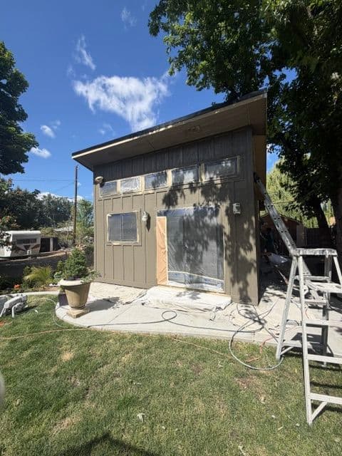 Modern home exterior renovation with a ladder, painting materials, and clear blue sky.