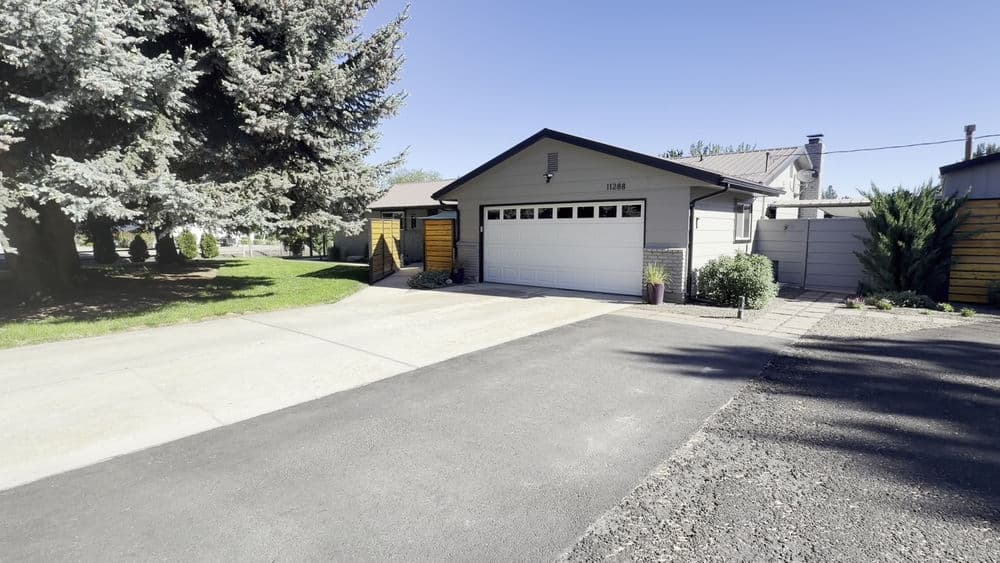 Modern gray house with garage, lush greenery, and spacious driveway. Scenic residential area.