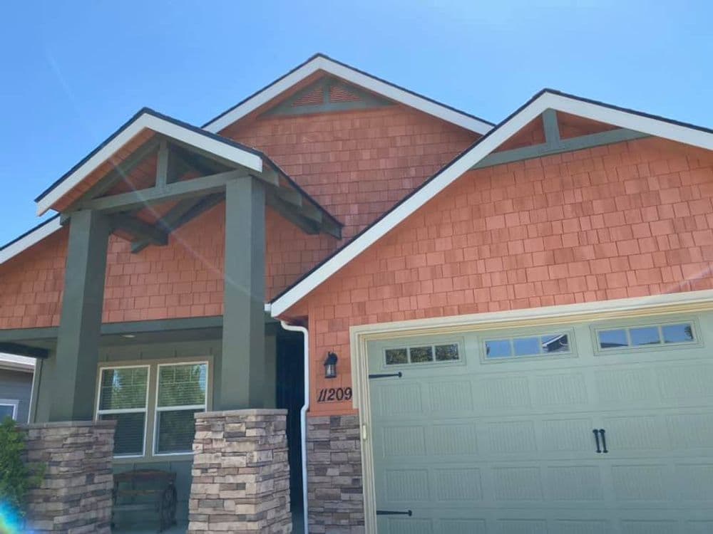 Modern house with orange shingles, stone accents, and a green garage door. Sunny day.