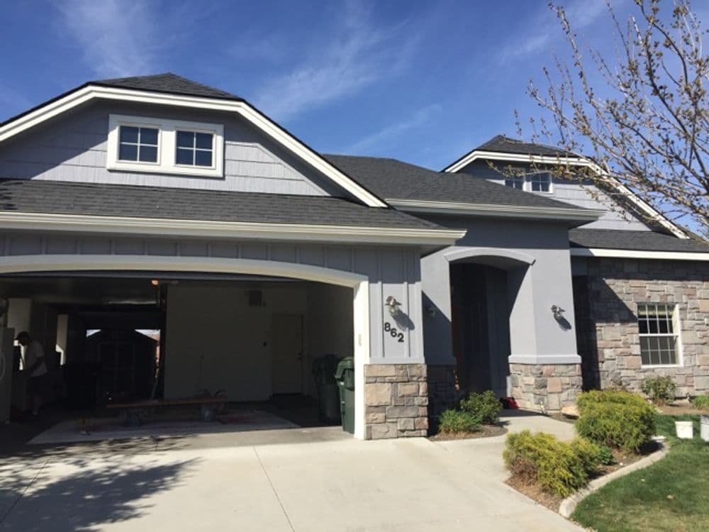 Modern suburban house with a stone garage and landscaped front yard on a sunny day.