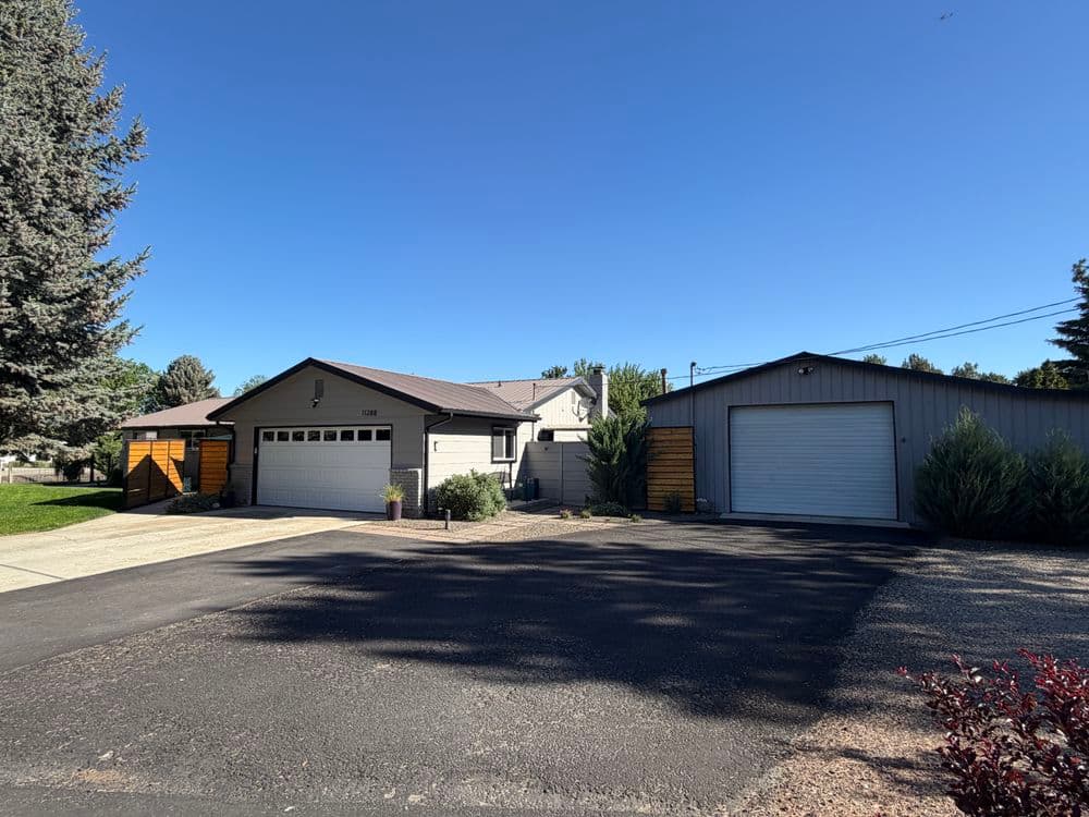 Modern house with garage and spacious driveway, surrounded by trees under a clear blue sky.