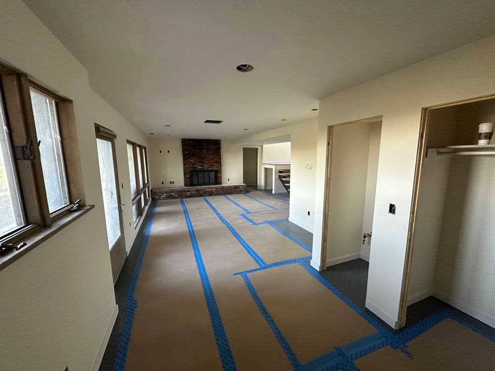 Spacious interior room with taped floors, fireplace, and light walls ready for renovation.